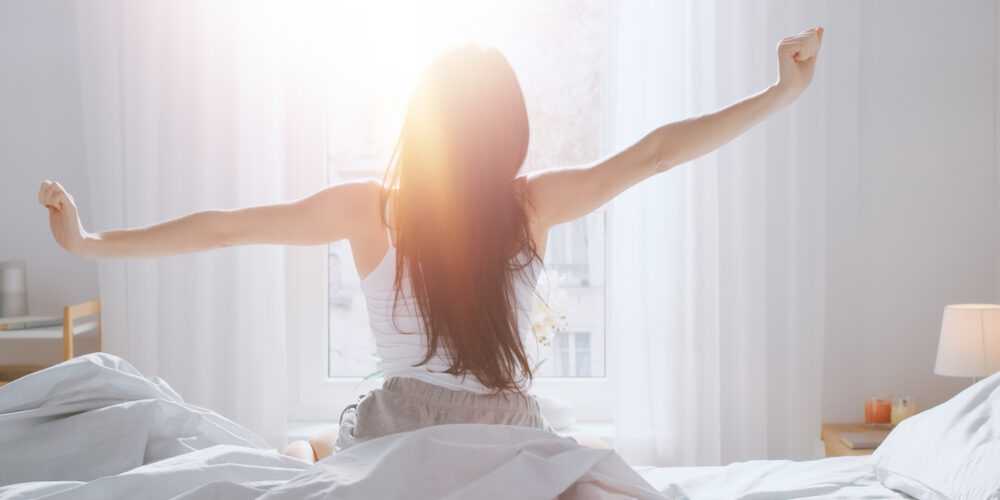女性がベッドに座って朝日を浴びている様子